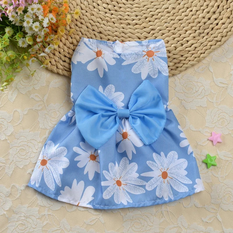 Blue spring dog dress with white flowers and blue bow. Background includes spring flowers.