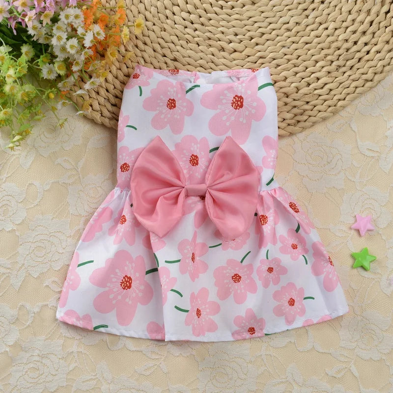 Pink spring dog dress with pink flowers and pink bow. Background includes spring flowers.