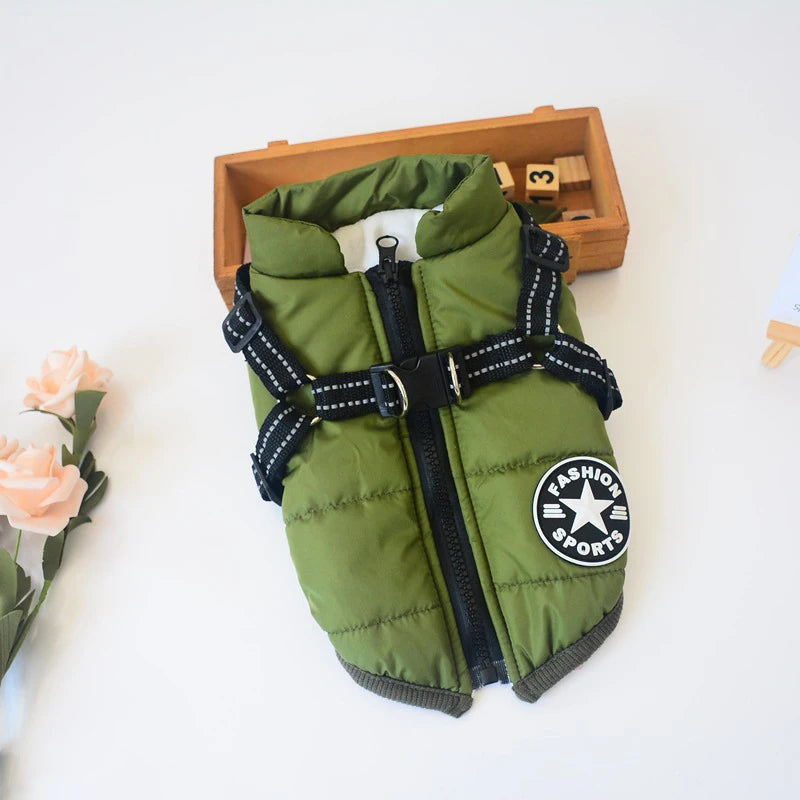 Green waterproof dog jacket with harness underside. Background includes flowers and toys.